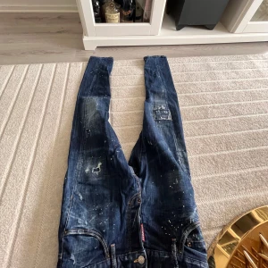 Dsquared2 jeans färgstänkta - Ett par mörkblåa (äkta) dsquared2 jeans med en unik färg combo. Färgstänkta i vit och grön samt blå med bra slitningar och feta detaljer. Knappt använda då de vart för små på mig ända sedan start, strl 44.