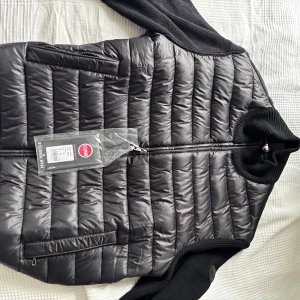 Svart cardigan jacka från Colmar - Säljer en svart cardigan jacka från Colmar med quiltad framsida och släta ärmar. Jackan har dragkedja framtill, två fickor med dragkedja och ribbad krage. Perfekt för dig som vill ha en stilren och sportig look.