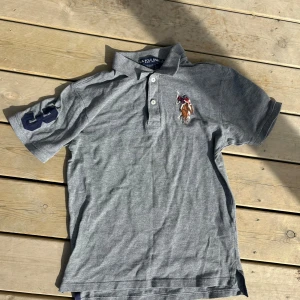 Grå pikétröja från U.S. Polo Assn. - Säljer en grå piketröja från U.S Polo Assn. xs-s i storleken, som ny, ligger bara i garderoben och kommer aldrig till användning. Perfekt till sommaren, pris kan diskuteras