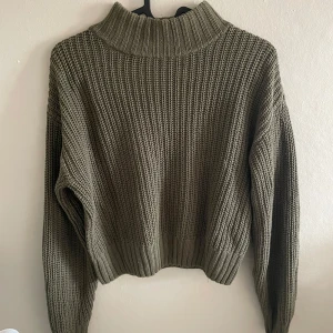 Olivgrön stickad polotröja - Säljer en olivgrön stickad polotröja med grov ribbad struktur. Tröjan har hög krage och långa ärmar, perfekt för kyligare dagar. Den är lite oversized i modellen och superbekväm att bära.