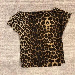 Leopardmönstrad topp - Säljer en snygg leopardmönstrad topp med korta ärmar och öppen rygg. Toppen har en tight passform och är tillverkad i ett stretchigt syntetmaterial. Perfekt för dig som vill sticka ut med ett djurmönster! 