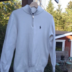 Vit stickad tröja med dragkedja från Ralph Lauren - Vit stickad tröja från Ralph Lauren med zip och klassisk broderad logga på bröstet. Tröjan har lång ärm och ribbade muddar vid ärmslut och nederkant. Perfekt för en stilren och avslappnad look. Skriv till mig om du har några funderingar pris kan också diskuteras.
