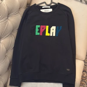 Svart sweatshirt från Replay med färgglad logga - Svart sweatshirt från Replay med REPLAY broderat i stora bokstäver på bröstet i svart, grönt, rött, gult, vitt och blått. Klassisk rund halsringning och långa ärmar. Nästan helt ny och använt i sparsamt sick ett fåtalt gånger. Storleken är Small men passar även medium. Ny pris på denna är 1199kr 