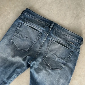 disel jeans med slitningar - Säljer ett par blå Disel jeans med snygga slitningar och lätt tvättad look. Klassisk femficksmodell med raka ben och normal passform. Jeansen har en liten detalj på myntfickan och är perfekta för en avslappnad stil.