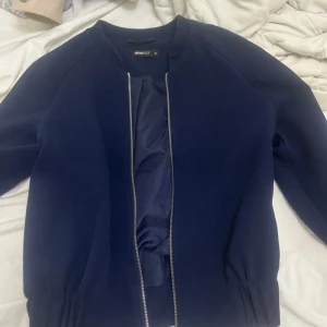Mörkblå jacka från Gina Tricot - Säljer en stilren mörkblå jacka från Gina Tricot i storlek 38. Jackan har dragkedja framtill. Perfekt inför våren samt hösten. 