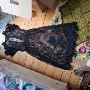 Svart långklänning i spets - Säljer en svart långklänning i transparent spets med v-ringning och korta ärmar. Klänningen har en romantisk känsla och är perfekt för dig som vill sticka ut. Passar till många olika tillfällen och är riktigt snygg att styla med boots eller klackar.