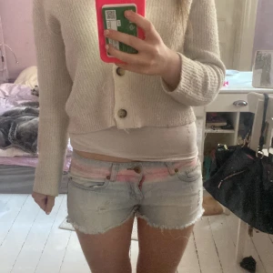 Ljusblå jeansshorts med rosa detaljer från Calzedonia - Säljer ett par ljusblå jeansshorts från Calzedonia med slitna kanter och rosa detaljer vid midjan. Shortsen har låg midja, klassiska fickor och råa benslut. Perfekta för sommaren!