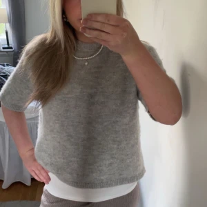 Ljusgrå stickad kortärmad tröja - Säljer en ljusgrå stickad tröja med korta ärmar. Tröjan har en rak passform och är mjuk och skön, perfekt för lager-på-lager. Enkel och stilren design som passar till mycket. Kan diskutera pris!