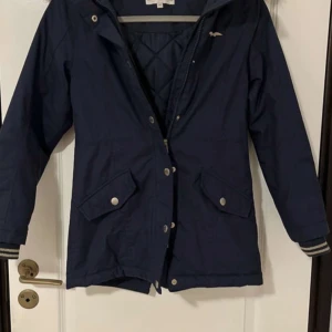 Marinblå parkajacka från Hampton Republic - Säljer en marinblå parkajacka från Hampton Republic med avtagbar huva och fuskpäls. Jackan har dragkedja och knappar framtill, två stora fickor och quiltat innerfoder. Perfekt för kyliga dagar.