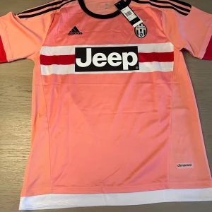 Juventus rosa fotbollströja Dybala 21 - Juventus fotbollströja i rosa med svarta och röda detaljer, Adidas-logga och Jeep som sponsor på bröstet. Dybala 21 tryckt på ryggen. Kortärmad modell i lätt och ventilerande climacool-material.