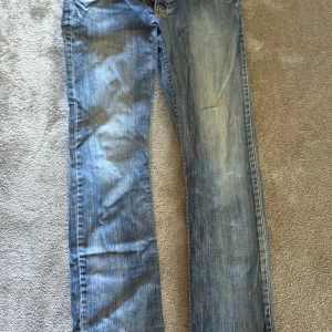 Blå jeansbyxor med raka ben - Säljer ett par klassiska blå jeansbyxor med raka ben och normal passform. Jeansen har fem fickor, knapp- och dragkedjegylf samt diskreta slitningar för en avslappnad look. Perfekta till vardags och lätta att matcha med olika stilar. Stil Dakota slim. Midjemått ca 42cm. Beninnerlängd ca 82cm. Längd ca 104cm. 