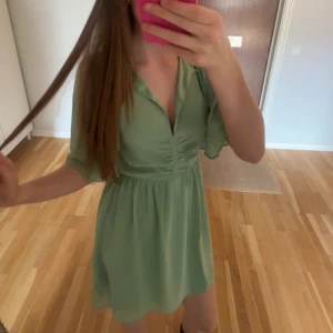 Ljusgrön kortklänning med v-ringning - Säljer en söt ljusgrön klänning med v-ringning och korta ärmar. Klänningen har en markerad midja och ett lätt, flowy tyg som passar perfekt till varma dagar. Perfekt för dig som gillar en enkel men stilren look.