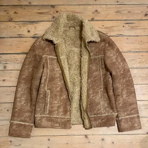 Brun pälsfodrad jacka med dragkedja - Säljer en brun jacka med mjukt, ljust teddyfoder och dragkedja framtill. Jackan har bred krage, två fickor och synliga sömmar. Perfekt för kyliga dagar och ger en retrovibe till outfiten.