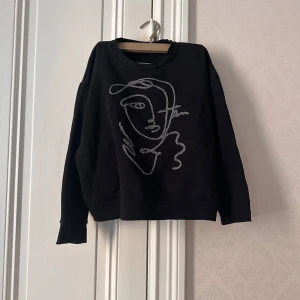 Svart sweatshirt med broderat ansikte - Svart sweatshirt från Zara  med ett stort broderat ansikte i grått på framsidan. Tröjan har rund hals och långa ärmar, samt en något croppad passform. Jättesnygg året runt och passar till allt!💗 storleken är M 