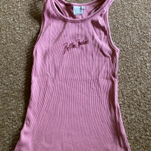 Rosa ribbad linnetopp från Better Bodies - Säljer en rosa ribbad linnetopp från Better Bodies med  logga framtill. Toppen har ärmlös design och rund halsringning, perfekt för träning eller sommarens varma dagar.