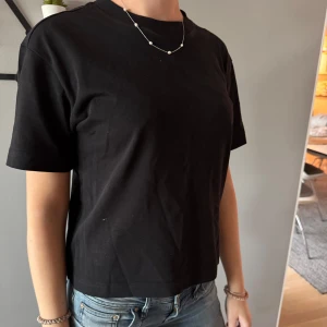 Svart croppad t-shirt - En enkel svart croppad t-shirt med rund halsringning och korta ärmar. Perfekt basplagg som passar till det mesta och är lätt att styla med olika accessoarer.