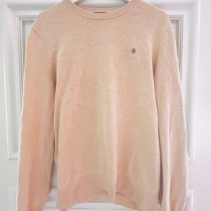 Beige stickad tröja från Morris - Säljer en stilren beige stickad tröja från Morris. Tröjan har rund halsringning, långa ärmar och en liten broderad logga på bröstet. Perfekt för lager-på-lager och enkel att matcha med olika outfits.