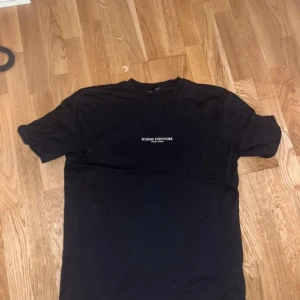 Svart t-shirt från New Yorker  - Säljer en svart t-shirt från New Yorker med vit text på bröstet och ryggen där det står 'ICONO COUTURE PARIS / TOKYO'. T-shirten har rund hals och normal passform. T-shirten har använts ca 3-5 gånger och den passar till det mesta och är väldigt skön att ha på sig. Storleken på T-shirten är Medium (M)