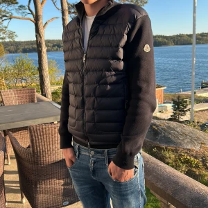 Svart pufferjacka från Moncler - Säljer en svart cardigan från Moncler med quiltad front och ärmar i mjukt tyg. Jackan har dragkedja framtill och Moncler-logga på ena ärmen. Perfekt för dig som vill ha en stilren och exklusiv look. Även en perfekt sommar jacka på kvällen. 