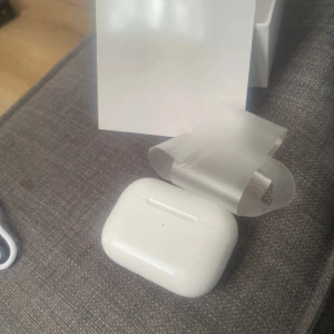 Hörlurar - Säljer ett par vita hörlurar med tillhörande trådlöst laddningsetui. Snygg och kompakt design i blank plast, perfekt för musik och samtal på språng. Levereras med originalförpackning.