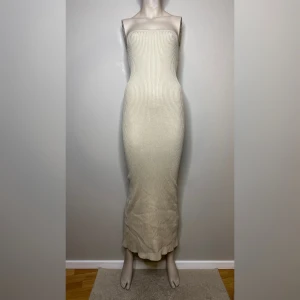 Beige ribbad långklänning från Bershka - Säljer en beige, ribbad långklänning från Bershka. Klänningen är axelbandslös och har en tight passform med slits baktill. 