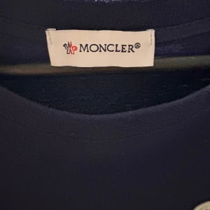 Mörkblå Moncler t-shirt  - Snygg mörkblå t-shirt från Moncler med klassisk rund hals och korta ärmar. T-shirten har en stilren look med Moncler-logga broderad på bröstet. Perfekt för dig som gillar exklusiva och enkla plagg. Materialet är mjuk bomull som känns skönt mot huden.
