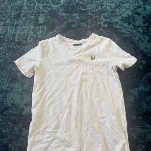Rosa t-shirt från Lyle & Scott Junior - Rosa t-shirt från Lyle & Scott Junior med klassisk passform och korta ärmar. På bröstet sitter den ikoniska gula fågel-loggan. T-shirten är gjord i mjuk bomull och har en enkel, stilren look som funkar till allt.