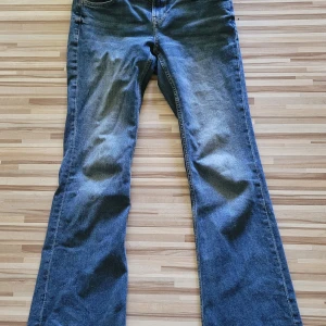 Blå bootcut jeans från Divided H&M - Ett par Snygga äldre vintage blåa bootcut jeans från Divided H&M i klassisk denim. Jeansen har normal passform, fem fickor och en lätt utsvängd benvidd. Perfekta för dig som gillar en retrovibe och vill ha ett par bekväma jeans med lite extra attityd.