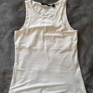 Vero Moda vit topp, storlek S. Nyskick - •Snygg vit topp från Vero Moda i slät och mjuk polyester.  •Sparsampt använd, nyskick. Tvättad. •Toppen är ärmlös med rund halsringning och har en enkel, stilren design som passar perfekt till jeans eller kjol.  •Lätt och luftig, perfekt för varma dagar. •Djurfritt och rökfritt hem.