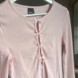 Ljusrosa ribbad topp med snörning - Supersöt ljusrosa långärmad topp från Gina Tricot med ribbad struktur och snörningsdetaljer framtill. Sitter tajt och har flera små rosetter längs öppningen. 🎀