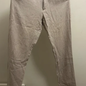 Beige linnebyxor från Riley slim fit - Snygga beige linnebyxor från Riley i slim fit-modell. Byxorna är tunna och lätta, perfekta för varmare dagar. De har en stilren look och är tillverkade i linne för en luftig känsla. Passar dig som gillar en smalare passform och enkel stil.