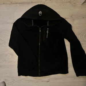 Marinblå zip hoodie från sail racing - Snygg marinblå zip hoodie från Sail Racing med dragkedja framtill och logga på bröstet. Jackan har huva med snörning och ribbade muddar. Perfekt för en chill och sportig look, funkar lika bra till jeans som till träningsbyxor.