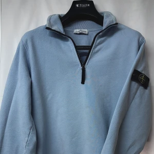 Ljusblå half zip från Stone Island - Ljusblå långärmad tröja från Stone Island. Den har ett bra skick. Går och använde på många sett! Köpt för ca 3000kr men kan ej hitta vad den kostar nu, därför säljs den för ett fair pris enligt mig! Junior storlek i small.
