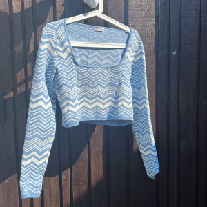 Blåvit croppad tröja från Stradivarius - Supersnygg croppad tröja från Stradivarius i blått och vitt med zigzag-mönster. Tröjan har lång ärm, fyrkantig ringning och är stickad i mjukt material. Perfekt att styla med jeans eller kjol för en trendig look.