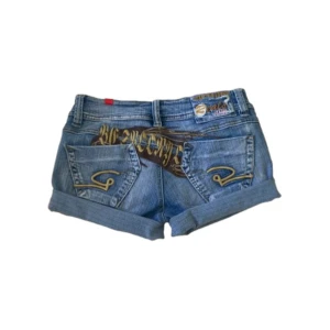  jeansshorts från Reals Jeans - Snygga blå jeansshorts från Reals Jeans med uppvikta benslut och coola broderade detaljer.    Gulfärgade sömmar och tryck på baksidan. Midjemåttet tvärs över är cirka 37 cm, materialet är lite stretchigt. Skriv för frågor! Ge prisförslag!!!!!