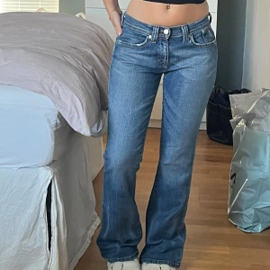 Low waist Levis bootcut jeans blå - Säljer ett par Levis jeans i klassisk blå tvätt. Modellen har låg midja och bootcut-ben, vilket ger en snygg retrovibe. Jeansen är i denim med fem fickor och Levis-logga på bakfickan. Perfekta för dig som gillar en avslappnad men ändå stilren look. Uppskattad storlek - XS/S, jag är 160 som referens!