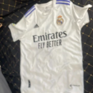 Real Madrid Benzema matchtröja Adidas - Säljer en vit Real Madrid fotbollströja från Adidas med Benzema och nummer 9 på ryggen. Tröjan har korta ärmar, klubbmärke på bröstet och blå detaljer på axlarna. Materialet är lätt och andas, perfekt för fotboll eller att bära som supporter.