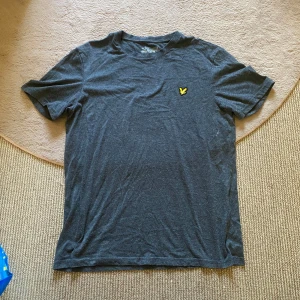 Mörkgrå t-shirt - Mörkgrå t-shirt från Lyle & Scott med klassisk passform och korta ärmar. På bröstet sitter den ikoniska gula örnloggan. T-shirten är gjord i mjuk bomull och har en enkel, stilren look som funkar till allt!🙌🏻Lite nopprig bara.