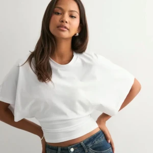 Vit topp från Nelly (ny) - Säljer en vit croppad topp med breda, korta ärmar och rund halsringning. Toppen har en tight passform över midjan och är gjord i mjuk bomull. Perfekt för dig som gillar en clean och stilren look.