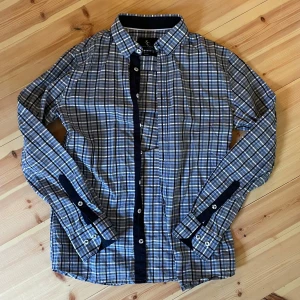 Rutig blå skjorta från Savvy Citizen - Snygg rutig skjorta från Savvy Citizen i blå, vit och beige. Skjortan har långa ärmar, klassisk krage och knappar framtill samt på manschetterna. Tillverkad i mjuk bomull och passar perfekt till jeans eller chinos.