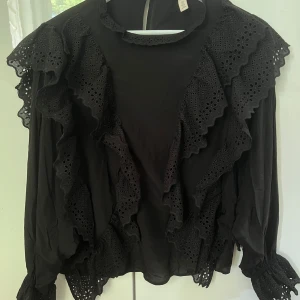 Svart blus med breda armar - En fin svart blus med volanger på framsidan och på slutet av ärmarna. På sista bilden kan man se att blusen är bred i armarna.