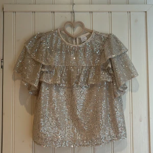 Glittrig volangblus från Lindex - Superfin glittrig blus/topp. Blusen/toppen är i jättefint skick då den är använd fåtal gånger. Storlek 158-164, säljer då den blivit för liten💕💕