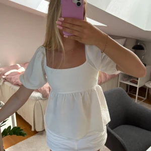 Vit blus med puffärm från Gina Tricot - Supersöt vit blus från Gina Tricot med puffärmar och fyrkantig ringning. Toppen har knytning i ryggen och en lätt strukturerad bomullskänsla. Nästan aldrig använd