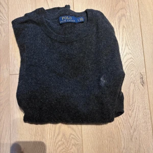 Mörkgrå ulltröja från Polo Ralph Lauren - Mysig mörkgrå tröja från Polo Ralph Lauren i mjuk ull. Klassisk rund halsringning och diskret broderad logga på bröstet. Perfekt för lager-på-lager och passar till allt. Enkel och stilren design som funkar året runt.