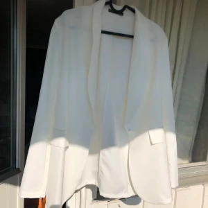 Vit kavaj med helt ny - Stilren vit kavaj med klassisk krage och en knapp framtill. Kavajen har två ilägg vid axlarna som ni ser på en av bilderna. Aldrig använd endast testad. Orginalpriset va ca 500kr