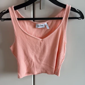 Rosa ribbad linnetopp - Supersöt ljusrosa/aprikos croppad linnetopp från Weekday med v-ringning. Toppen är ribbad och ärmlös, perfekt för varma dagar. Mjuk och stretchig bomullskänsla som sitter snyggt och bekvämt. Enkel att matcha med både jeans och kjol.