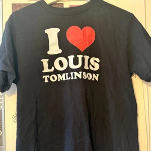 Svart I Love Louis Tomlinson t-shirt - Svart t-shirt med tryck 'I ♥ Louis Tomlinson' i vitt och rött framtill. Klassisk rund hals och korta ärmar. Köpt på Etsy och använd 1 gång.