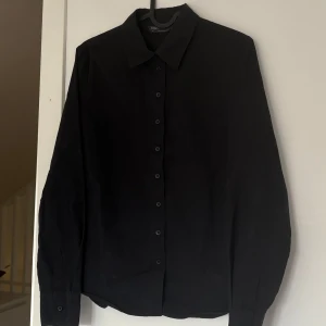 Svart skjorta från M&S  - Klassisk svart skjorta från M&S i storlek 38. Skjortan har lång ärm, knappar hela vägen framtill och en stilren krage. 
