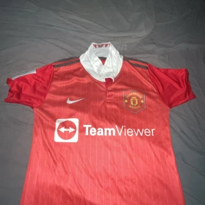 Manchester United Ronaldo 7 matchtröja - Manchester Uniteds officiella matchtröja med Ronaldo 7 på ryggen. Röd med tunna vita ränder, vit krage och klubbmärke på bröstet. Nike-logga och TeamViewer sponsortryck. Tillverkad i lätt och ventilerande material, perfekt för fotboll eller supporterliv.