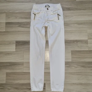 Vita jeansbyxor med dragkedjor, Kids 140 - Snygga vita jeansbyxor från Lindex Kids i storlek 140. Byxorna har guldiga dragkedjor framtill, klassisk femficksdesign och knapp i midjan. Perfekt för dig som gillar stilrena och fräscha plagg med coola detaljer.